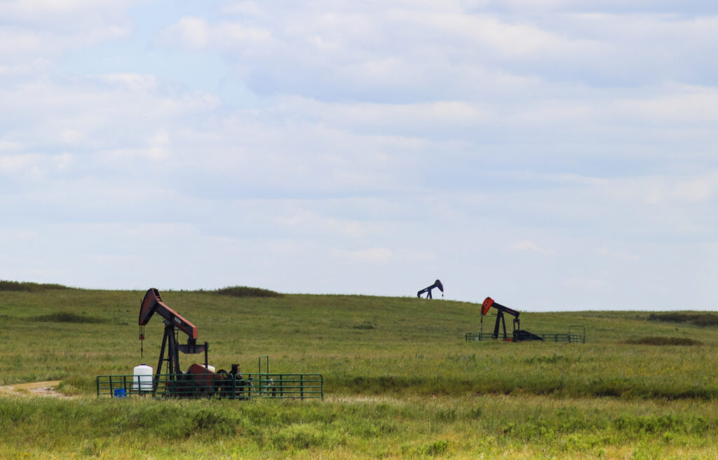 Three working pump jacks on oil or gas wells out in a green field 