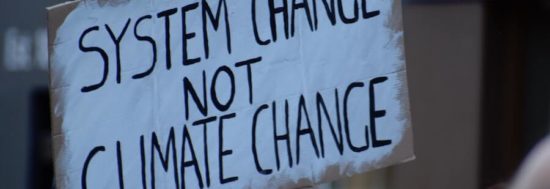 a protest poster reads "system change not climate change"